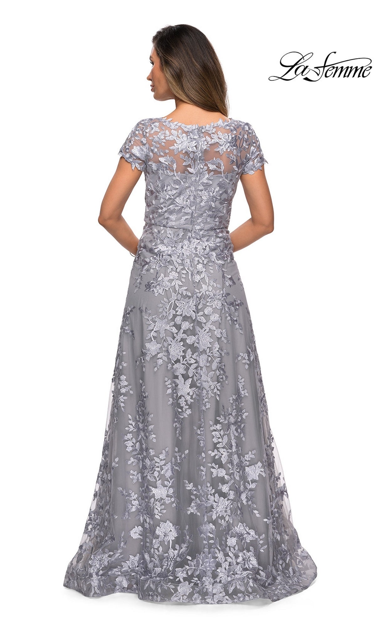 Woman in a silver-gray floor-length gown with short sleeves and a floral lace overlay, shown from the back. The Long Formal Dress: La Femme 27870 offers a graceful silhouette, making it an elegant choice for special occasions such as mother of the bride events.